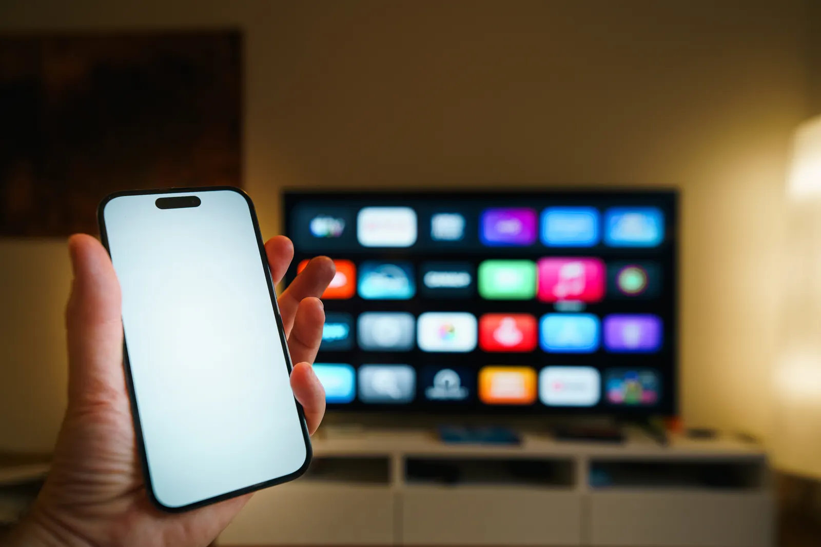 A hand holding a phone with the DuoSmart playlist page, a TV with the app in the background